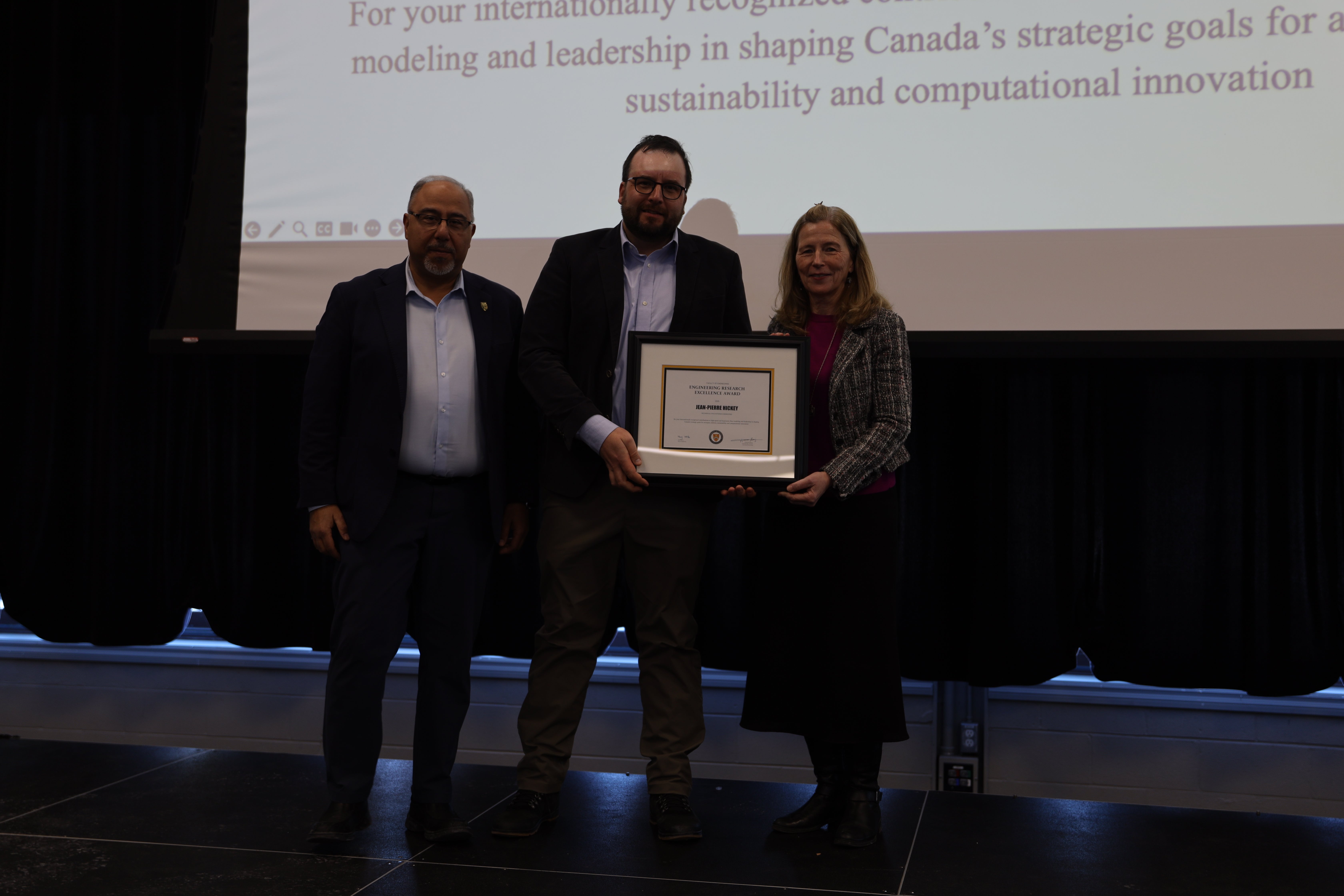 Two men and  one woman pose with a certificate on stage.