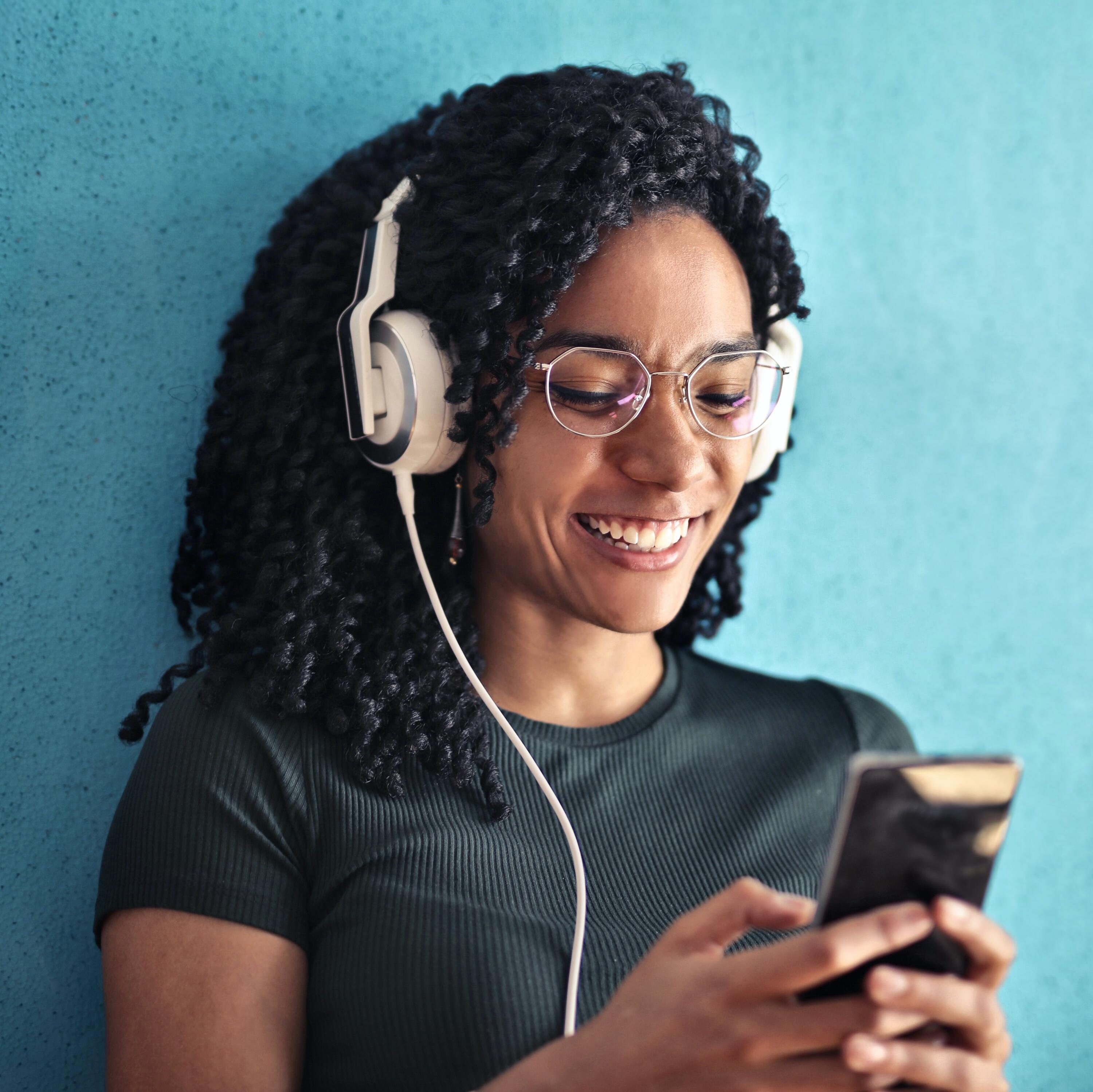 Picture of woman leaning against wall listening to app on her phone