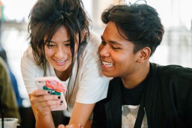 two teenagers looking at a phone and smiling
