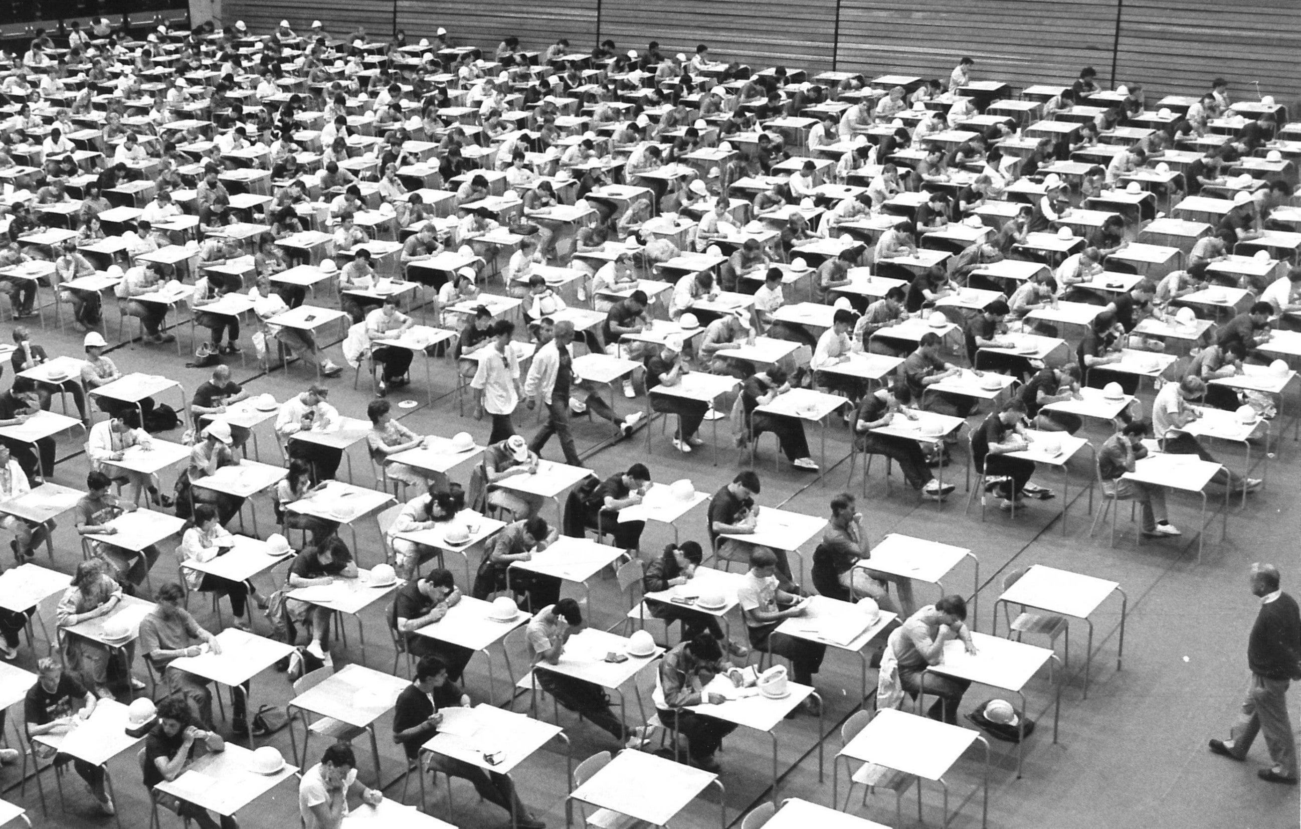 Students at exam tables in neat rows writing exams.