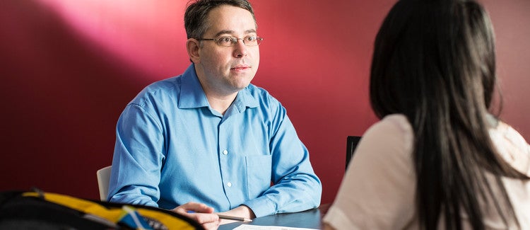 A photo of a male professor advising a female student at a desk