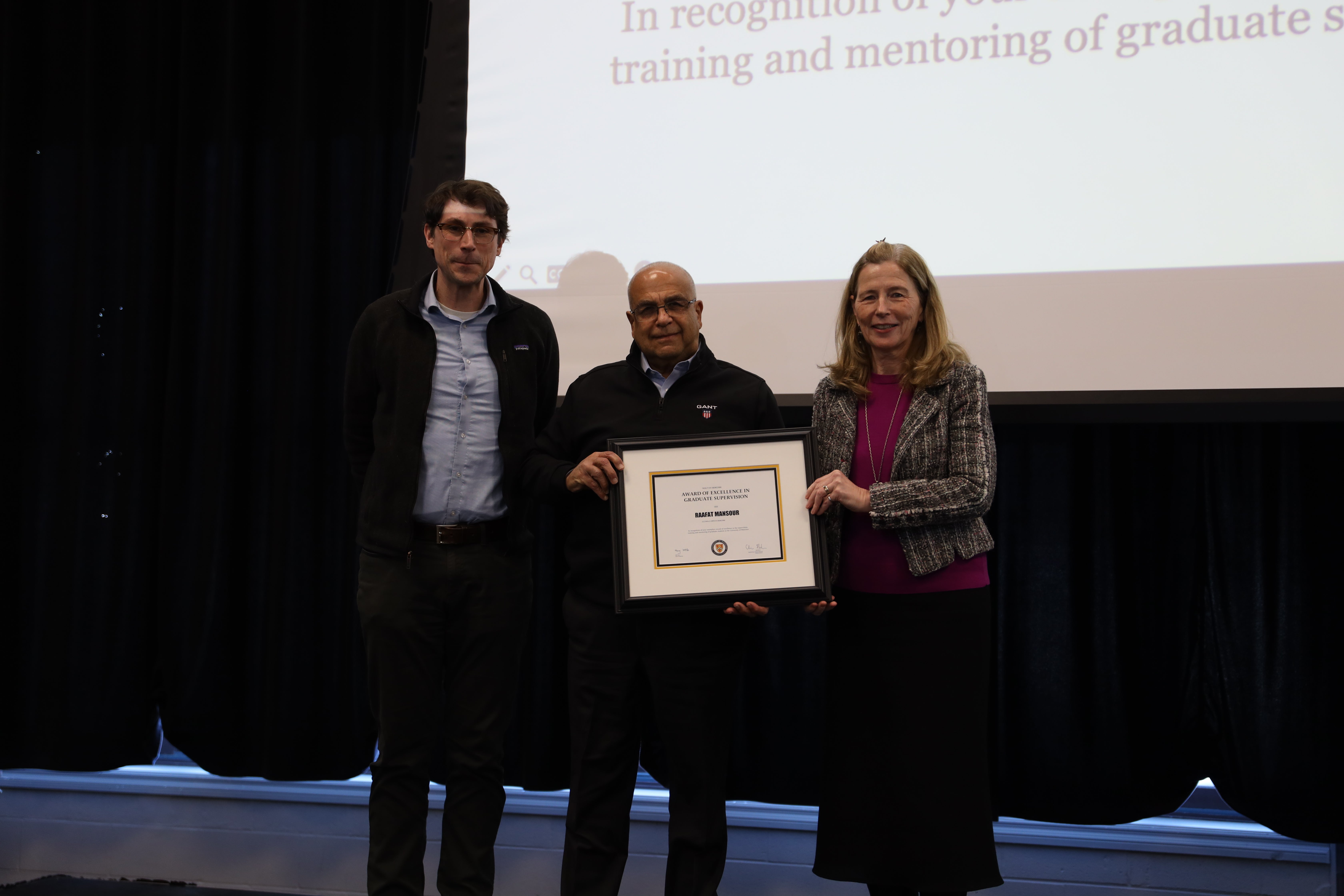 Two men and one woman pose on stage with a certificate.