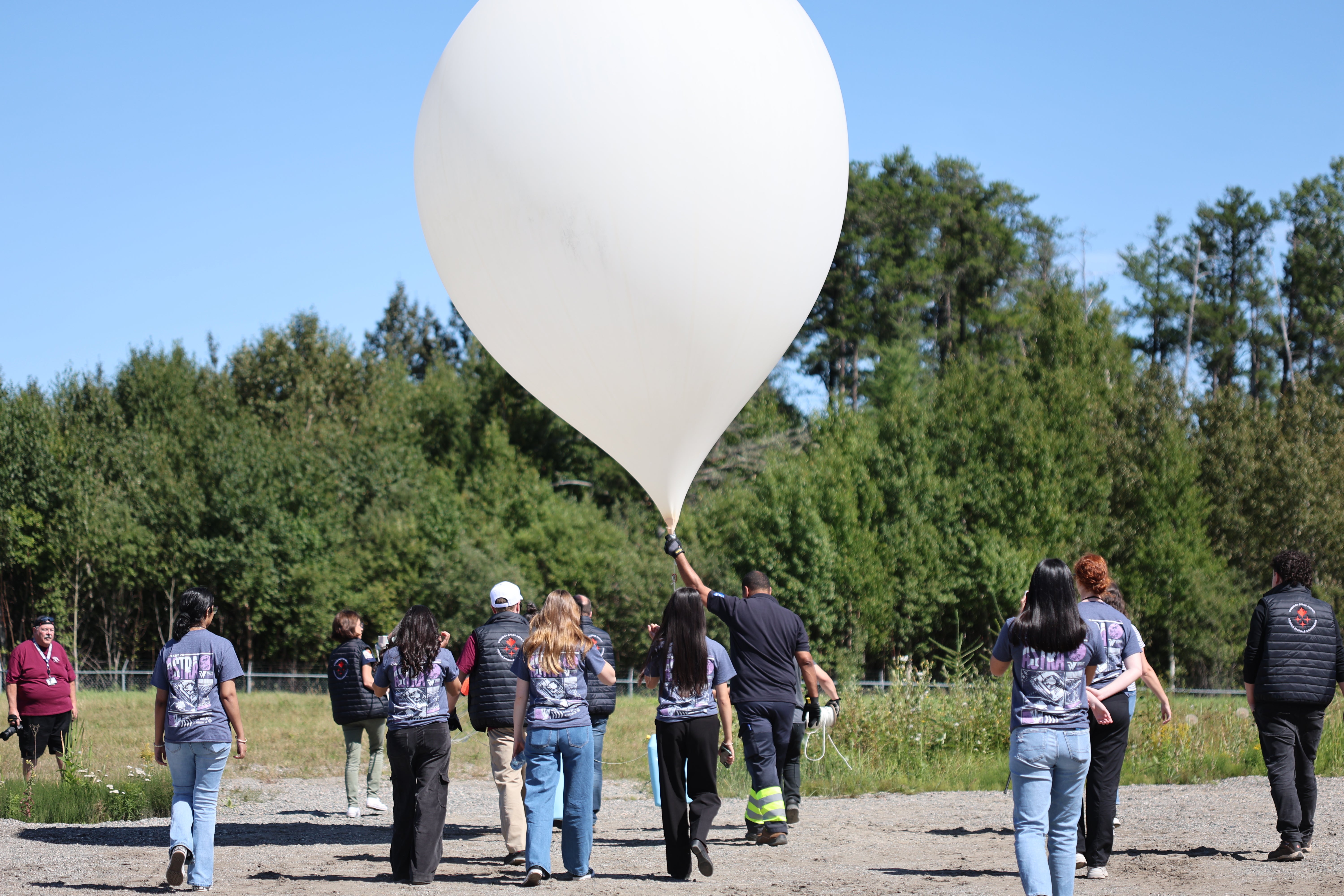 A group of students walk their large, inflated balloon out into an open field for launch.