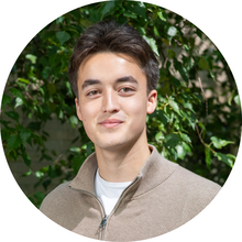 A young man looks at the camera in front of a tree