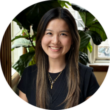 A young woman smiles at the camera in front of a tree