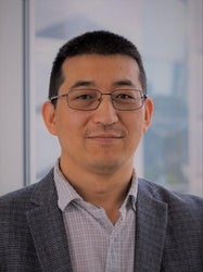 A man with glasses smiles at the camera in front of a window.