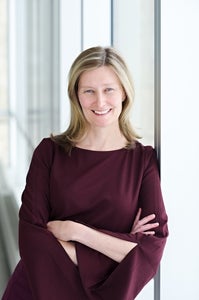 A woman leans against a wall and smiles at the camera