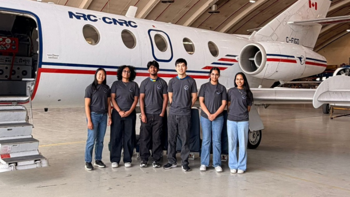 Students pose in front of an airplane in an airport hangar.