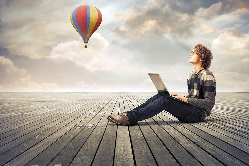 Photo of writer with laptop with hot-air balloon in background.
