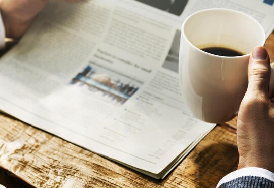 reading a newspaper, holding a coffee