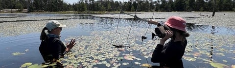 two people chest-deep in a wetland lake holding an antenna