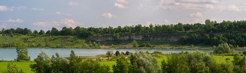 Kelso quarry wide view. treestops in foreground, lake and grasses and trees behind, light clouds in the sky