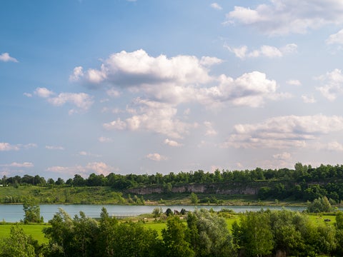 wide view of Kelso Conservation area with treetops on the foreground, a small lake and vegetation and trees with a cliff in the background