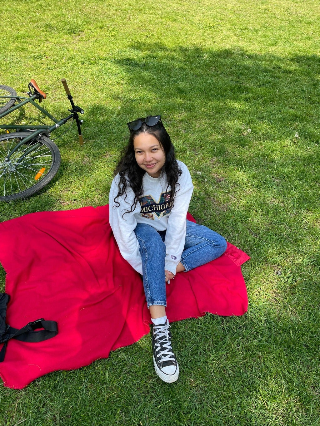 woman sitting on a red blanket on a grassy area. A bicycle is on the ground nearby.