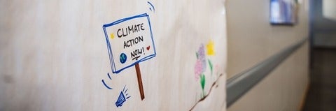 a protest style sign saying Climate Action Now is drawn on a white board. A drawing of some flowers is nearly.
