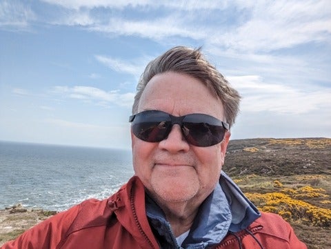 Stephen Murphy wearing sunglasses with an ocean on the left and low lying vegetation on the right.