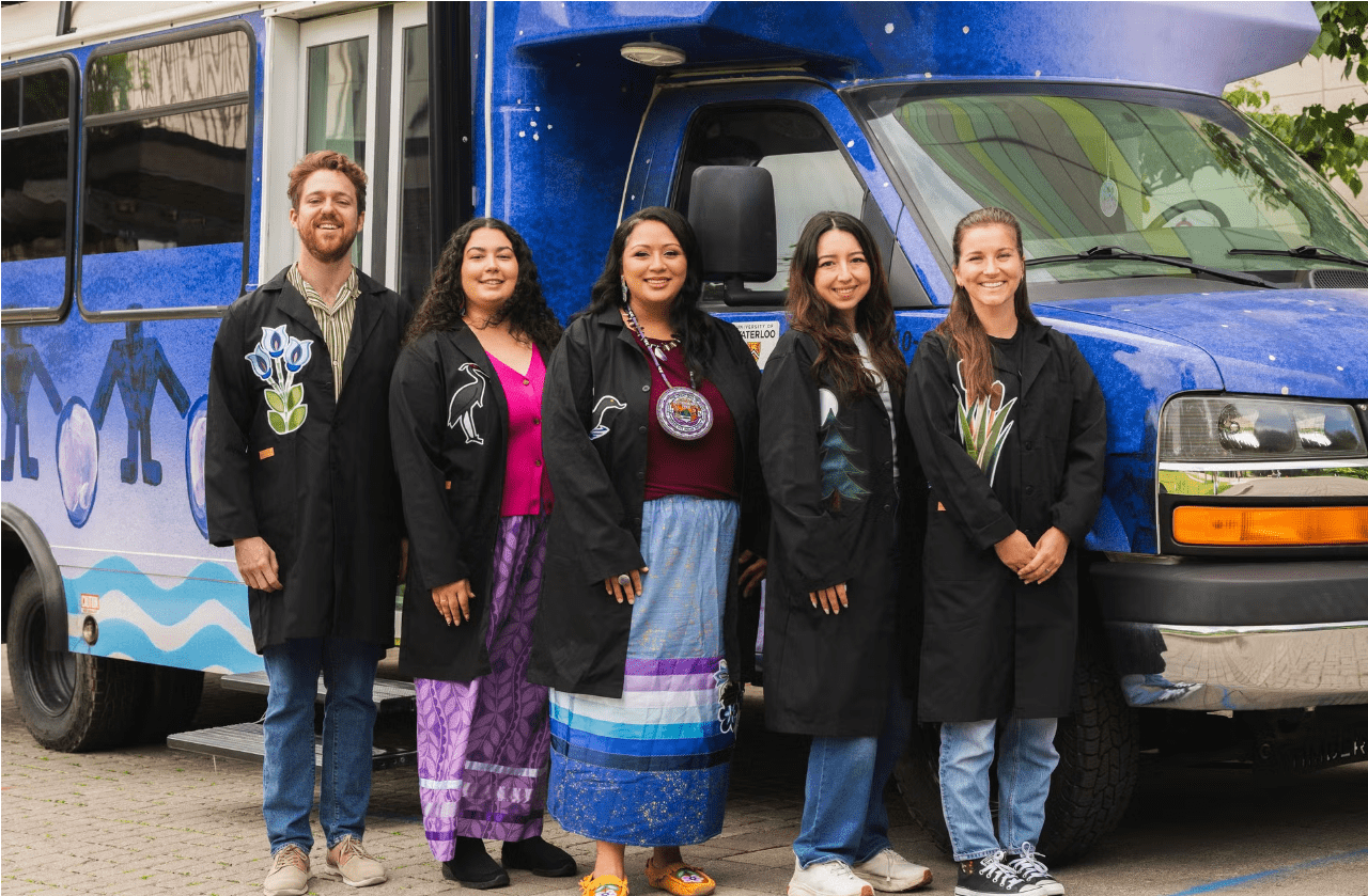 Kelsey Leonard and team stands beside the WAMPUM lab mini-bus which is brightly painted with Indigenous artwork