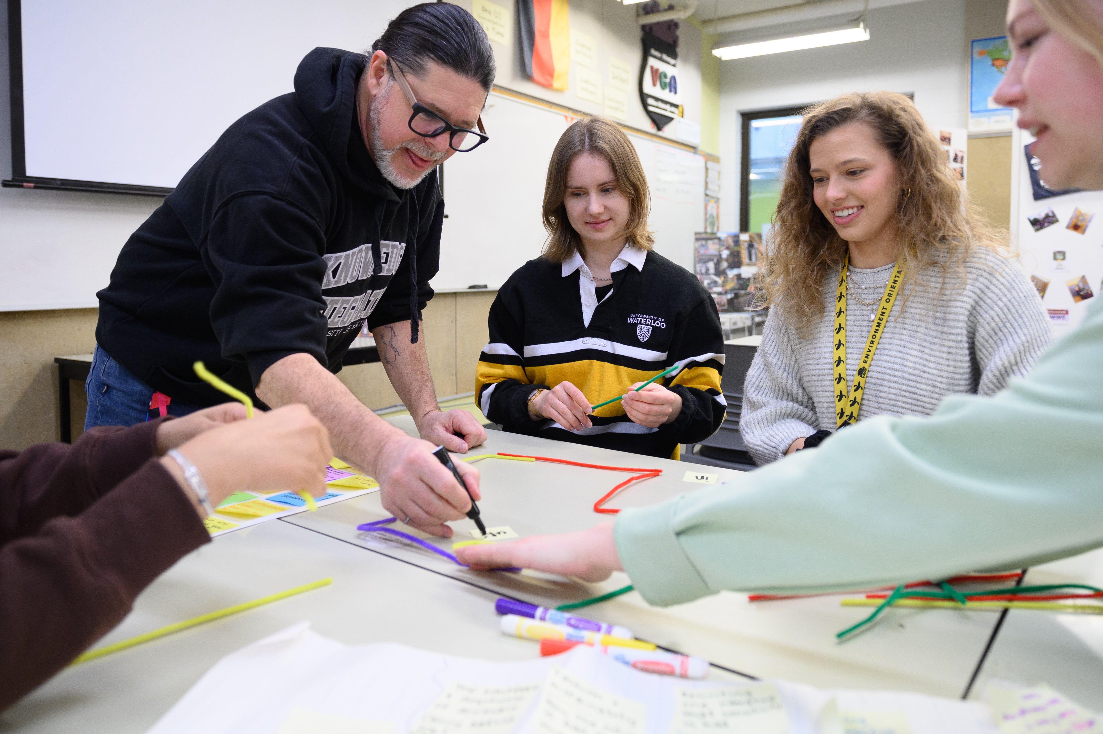 three students interact with an instructor around a table while using sitcky notes