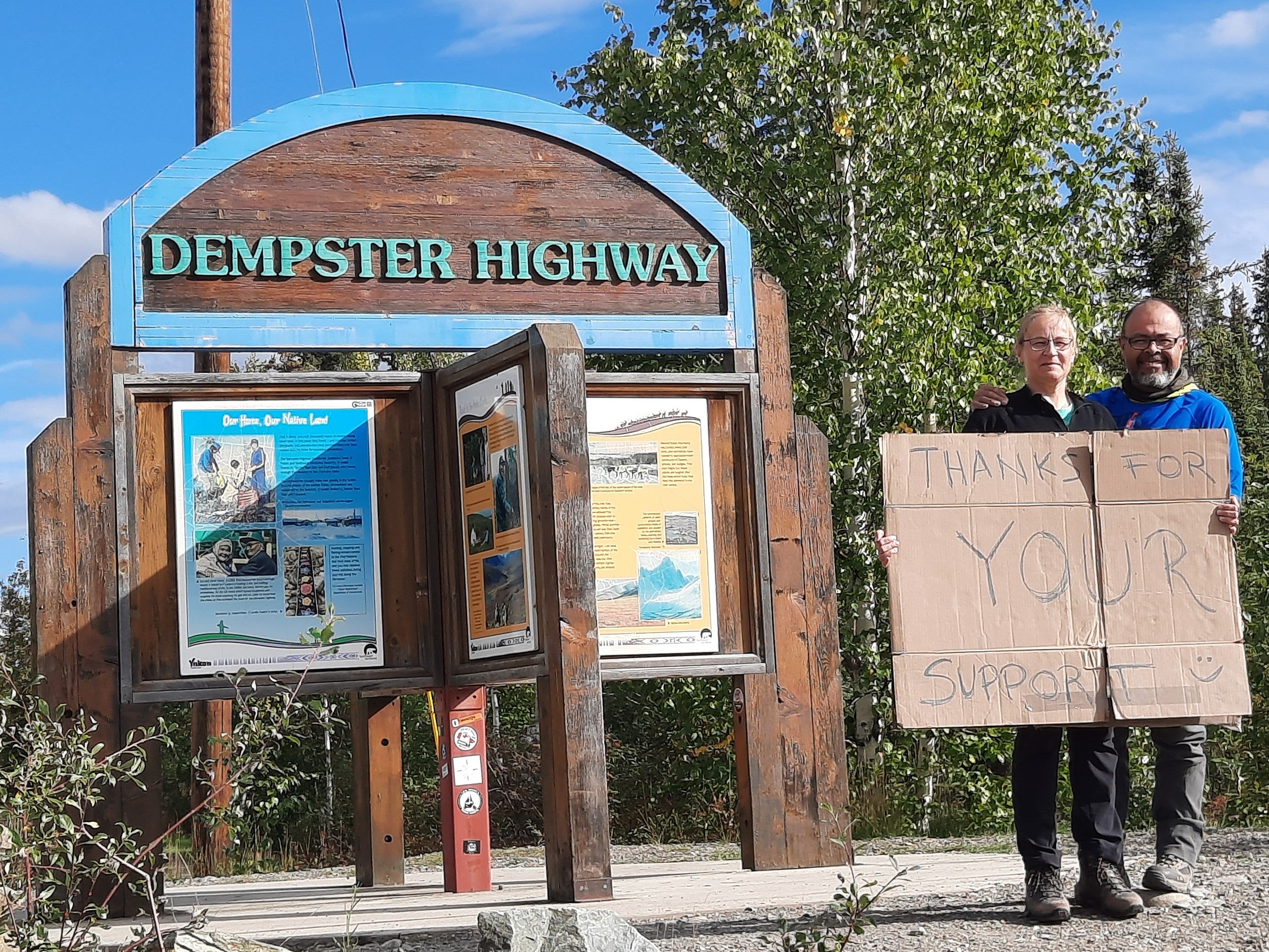 Maren Oelbermann and Pedro Gonzalez Hernandez hold a sign saying Thanks for your support, at the sign marking the start of the Dempster Highway.