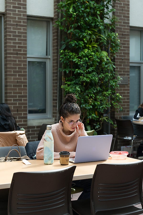 University student sitting at a table looking at a laptop computer screen in Environment Courtyard