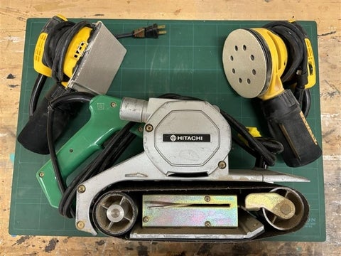 A sheet sander, random orbital sander and belts sander on a table.