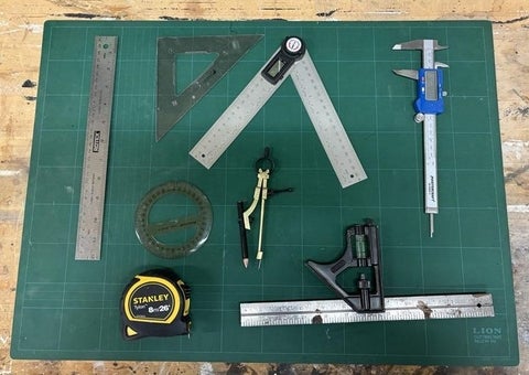 Rulers, protractor, measuring tape and calipers displayed on a table.