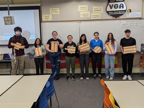 8 students lined up holding the cutting boards they made.