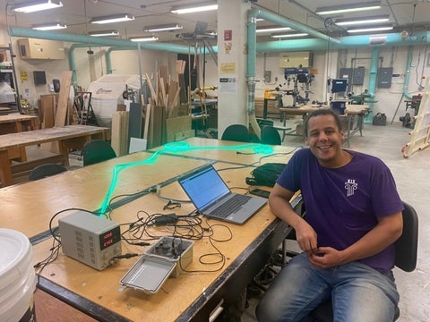 Someone smiling, sitting beside a table with a laptop and light strip air quality device.