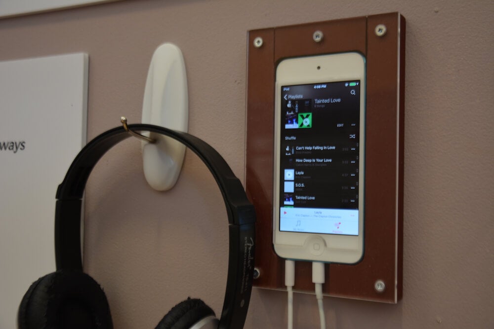 A phone case secured to the wall, with an iPhone inside and a headphone next to it.