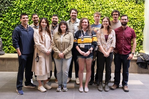 A diverse group of eleven people stand in front of a vibrant green living wall, posing for a group photo.