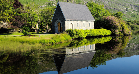Ancient stone building at edge of reflective pool, with cliff face in the background