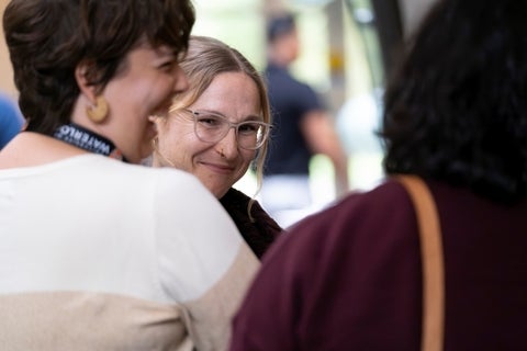 Close-up shot of three individuals in a semi-circle, with two faces in sharp focus and one in soft focus from behind, appearing engaged in a conversation in an indoor setting.