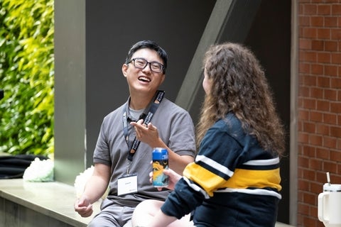 A man wearing glasses and a grey polo shirt with "Waterloo Alumni" lanyards smiles and gestures while talking to a woman with curly brown hair wearing a blue and yellow striped sweater.