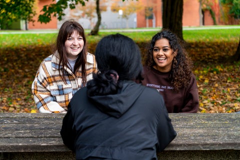 Three students sitting on a picnic table.