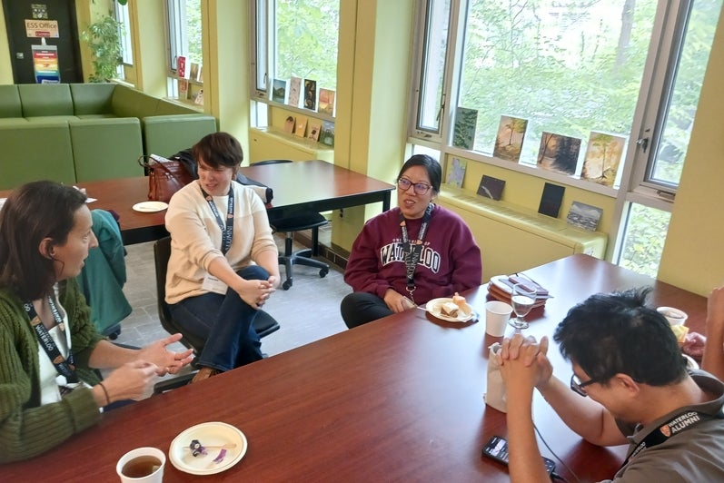 A group of four people sit at a table with coffees, talking. 
