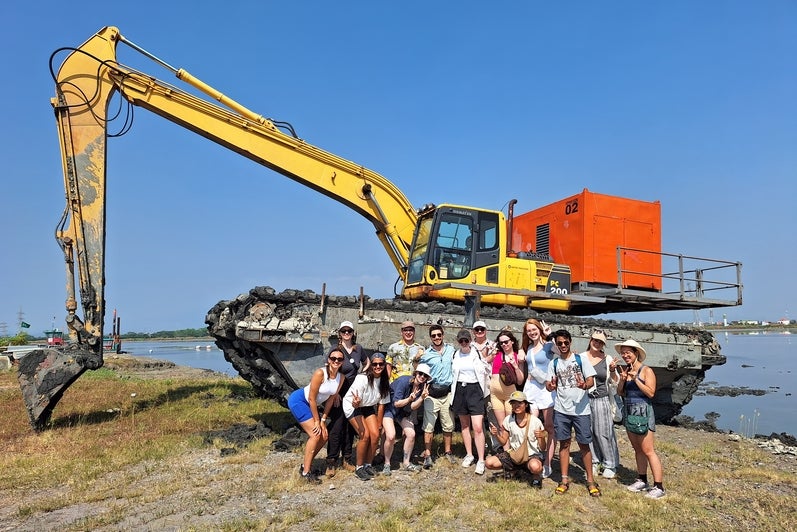 Group of students and professor in front of heavy machinery.