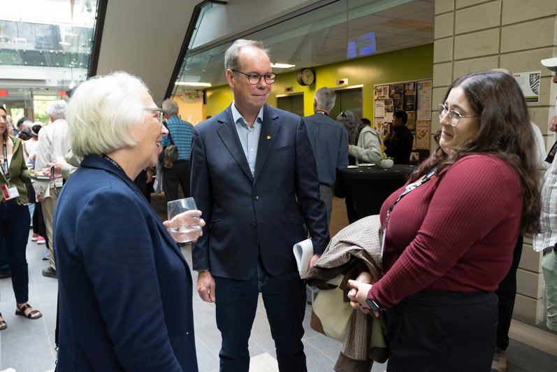 A group of people engaged in conversation, with one individual holding a drink and smiling.