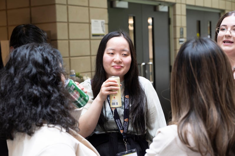 A group of people engaged in conversation, with one individual holding a drink and smiling.