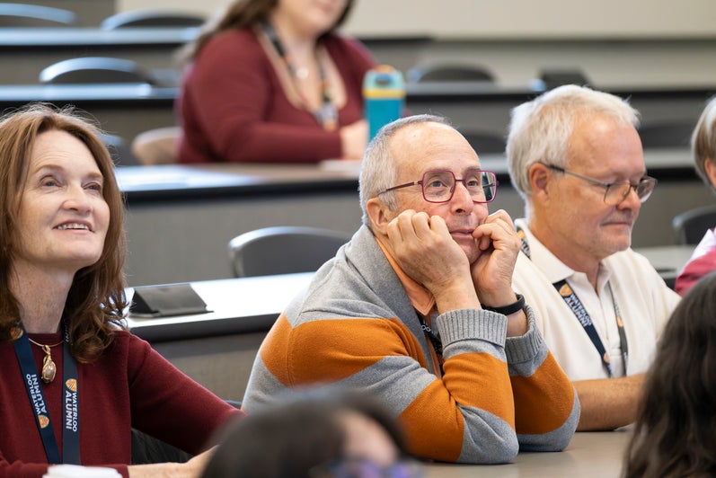 A group of people sitting in a classroom or lecture hall, listening attentively.
