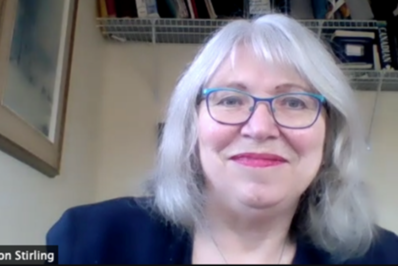 Woman with shoulder length grey hair and glasses smiles.
