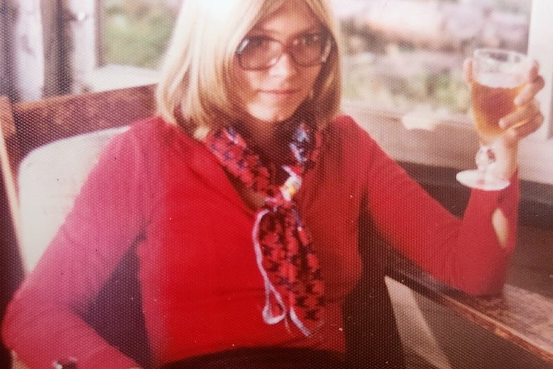 Young blond woman in red sweather with scarf hold a wine glass.