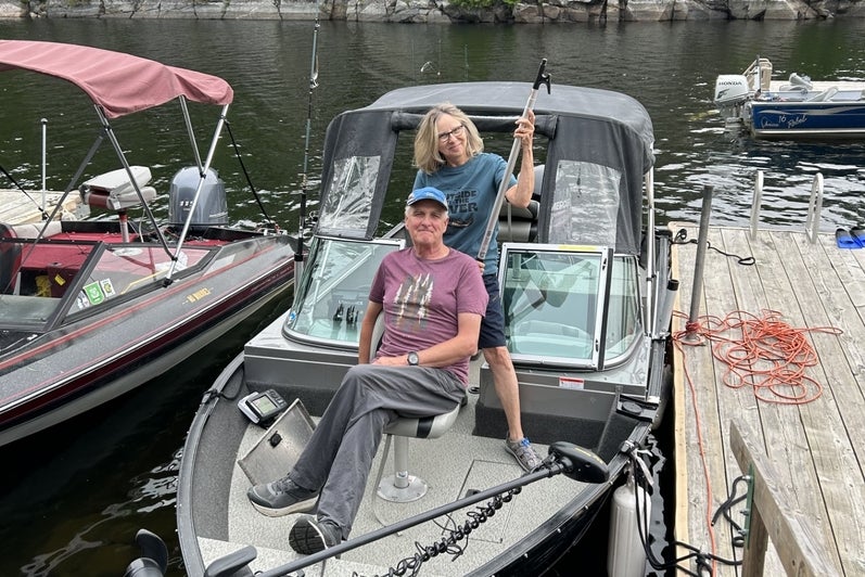 Man in ballcap and woman in blue tshirt smile from a fishing boat at a dock.