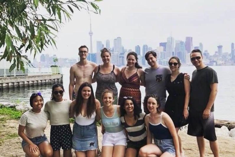 Group of university students smiling at a beach with the Toronto skyline behind them