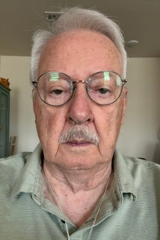 Older man with glasses and grey hair looks ahead.