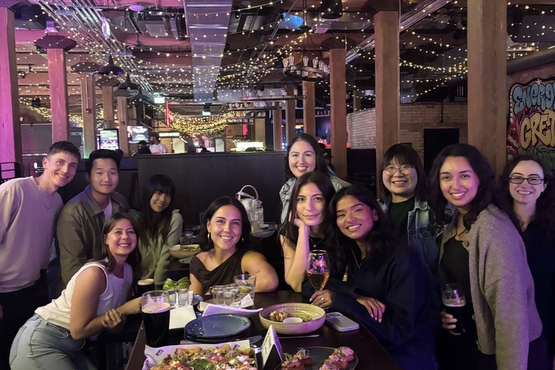 A diverse group of people posing together at a table in a lively restaurant with dim lighting and decorations.