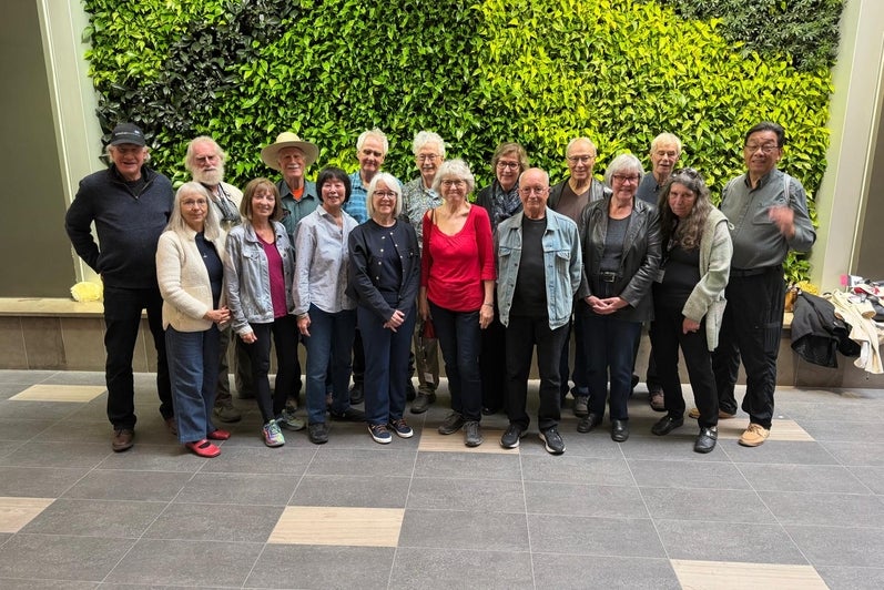 A group of people standing together in front of a green wall made of plants.