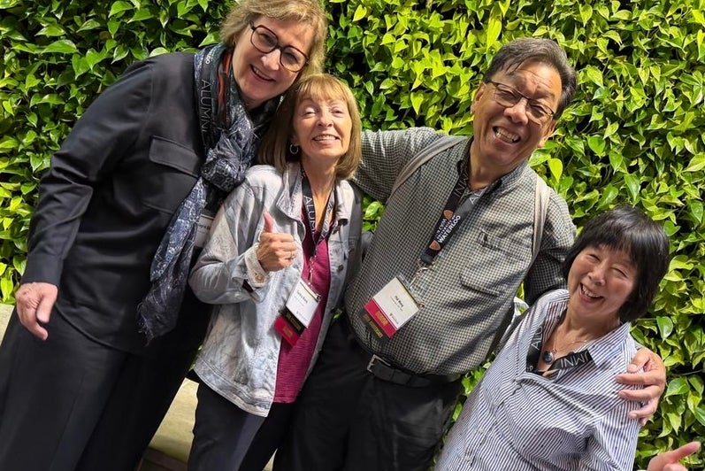 Four people posing together in front of a green wall.