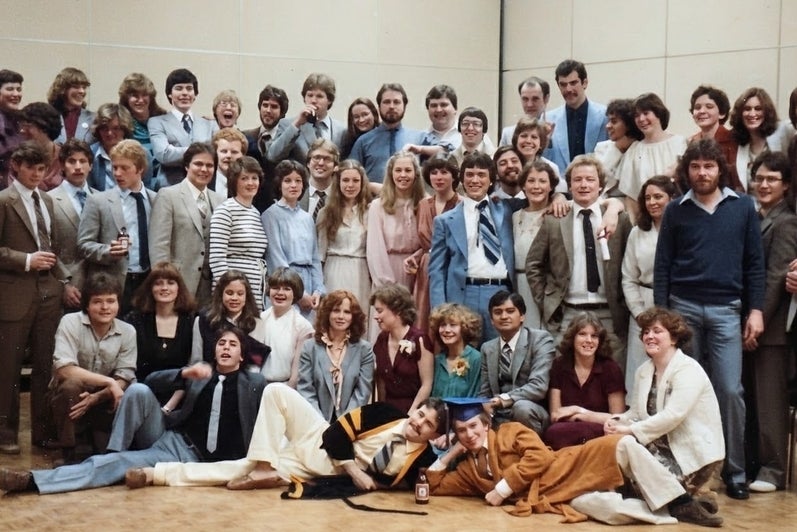 A large group of people gathered for a photo, dressed in a mix of formal and casual attire, with some wearing suits and others in dresses.