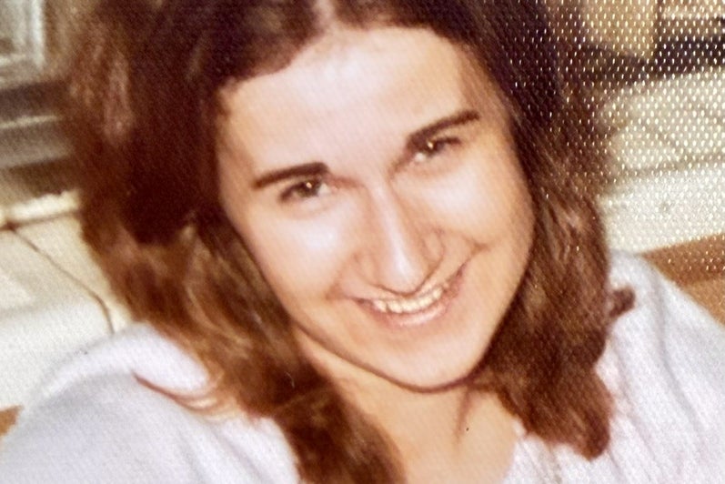 Woman with brown hair and white top smiles with head to one side.