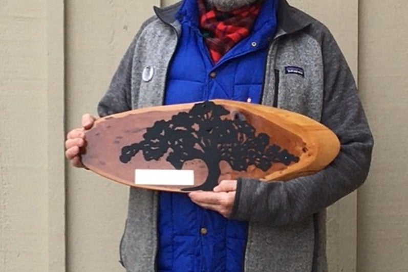 Man with grey hat and glasses holds plaque.